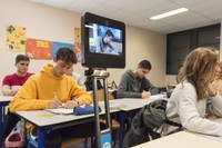 Photo montrant une classe de lycéens en train de prendre des notes pendant un cours et au premier plan un élève apparait sur l'écran du robot de téléprésence en train de faire de même
