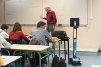 Photo montrant un professeur donnant cours à une classe de lycéens, avec la présence du robot de téléprésence au premier rang à côté du bureau d'un élève